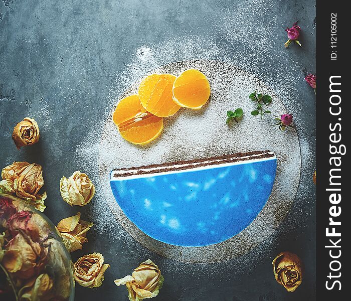 Half of cutted mousse cake with blue glaze on a dark gray concrete background