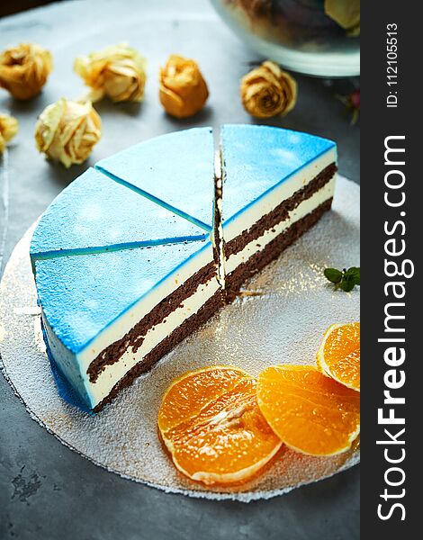 Half of cutted mousse cake with blue glaze on a dark gray concrete background