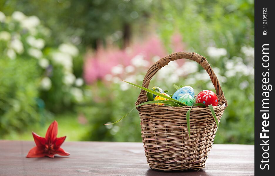 Basket with painted eggs and red lilly flower on table in garden