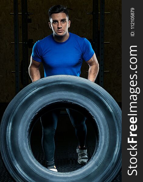 Portrait of a strong athlete with a large heavy wheel in the gym