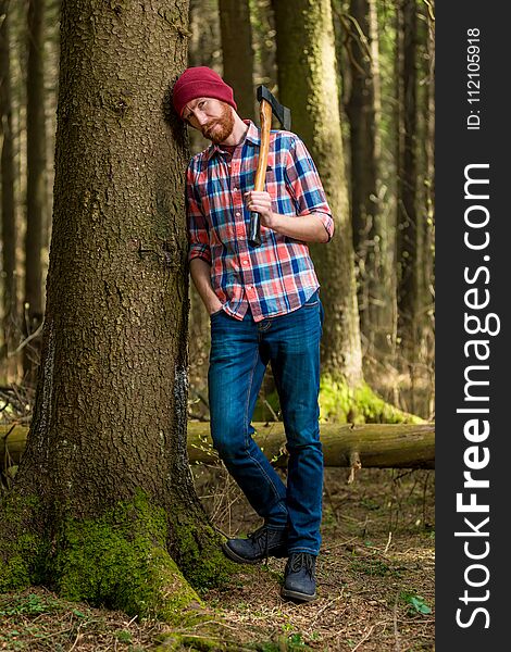 Tired bearded lumberjack with an ax resting, leaning against a tree