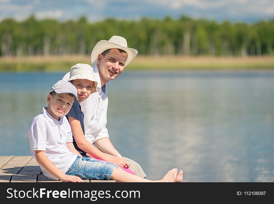 Portrait Of Father And Children Sitting On A Wooden Pier