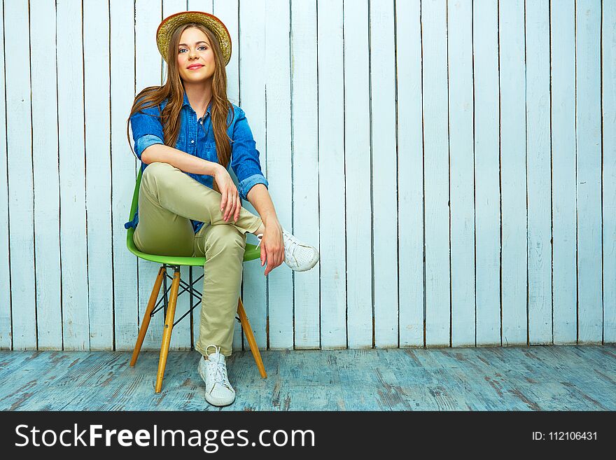 Hipster style young woman sitting on chair. Full body portrait of smiling girl.