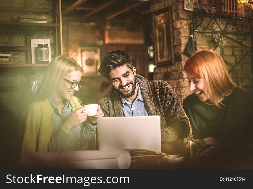 Three young smiling student using laptop together at cafe. Small group people. Three young smiling student using laptop together at cafe. Small group people.