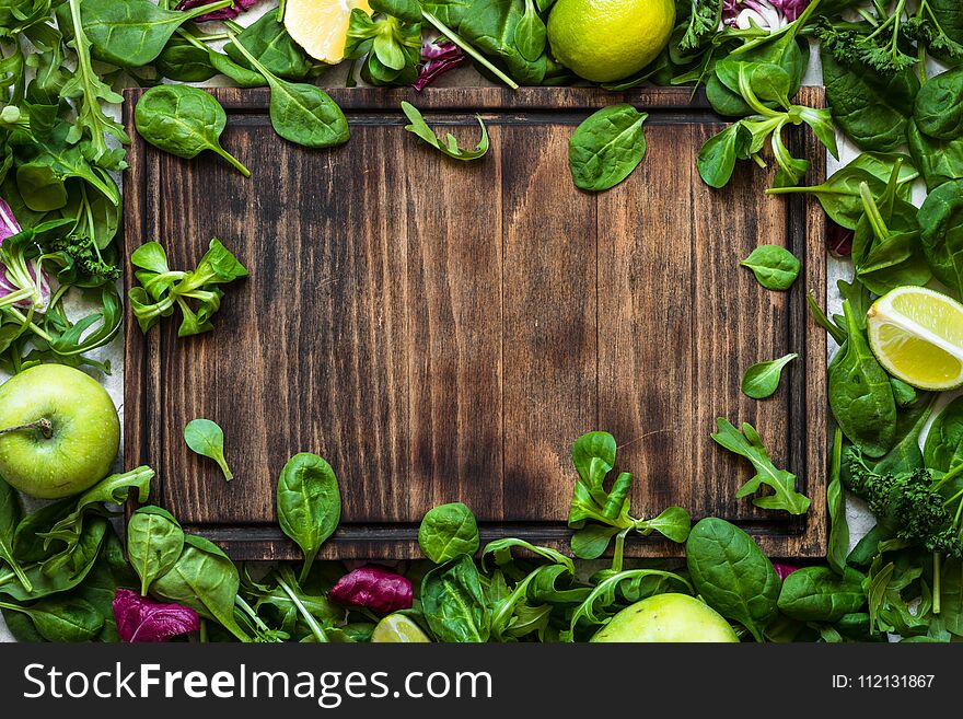 Green food background. Salad ingredients on table with cutting board and copy space. Healthy food and diet concept.