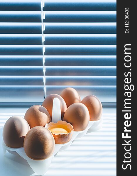 Chicken eggs on the background of blinds through which sunlight breaks. With a broken egg. Chicken eggs on the background of blinds through which sunlight breaks. With a broken egg.