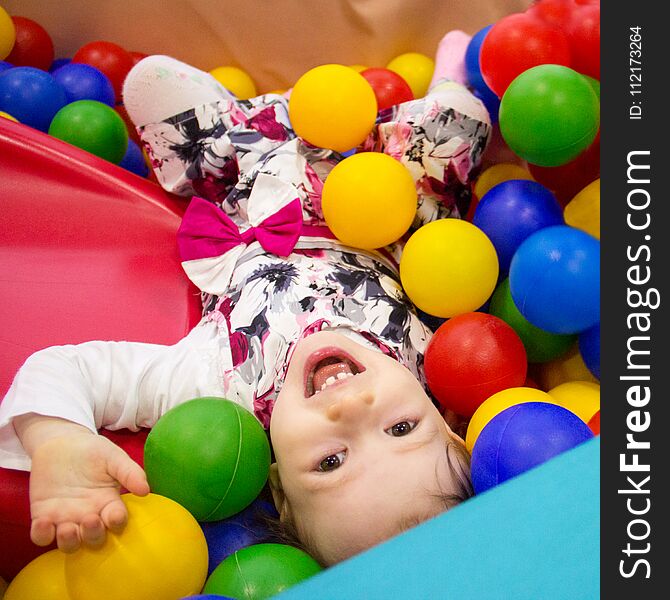 Little cute smile girl plays in balls for a dry pool. Play room. Happiness