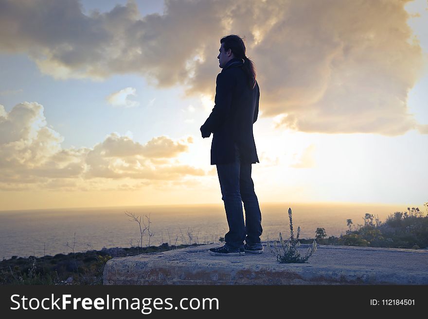 Man Wearing Black Coat Standing Near Sea during Golden Hour
