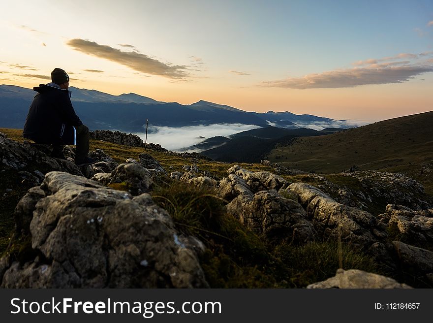 Person In Black Hoodie Sitting On Gray Stone