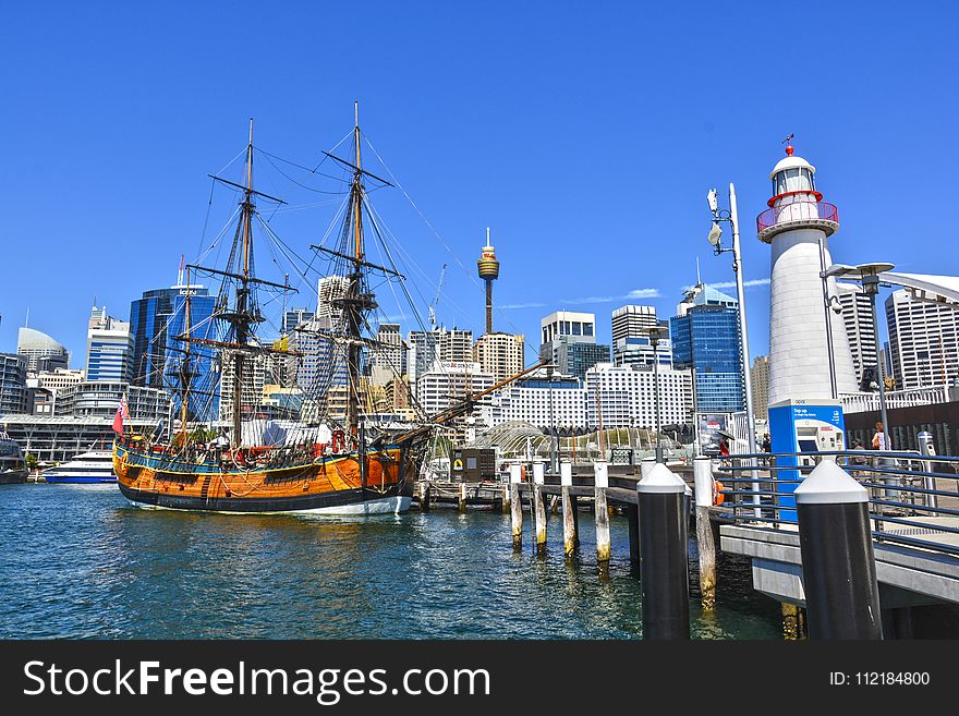 Orange Galleon Ship On Body Of Water Beside City Buildings