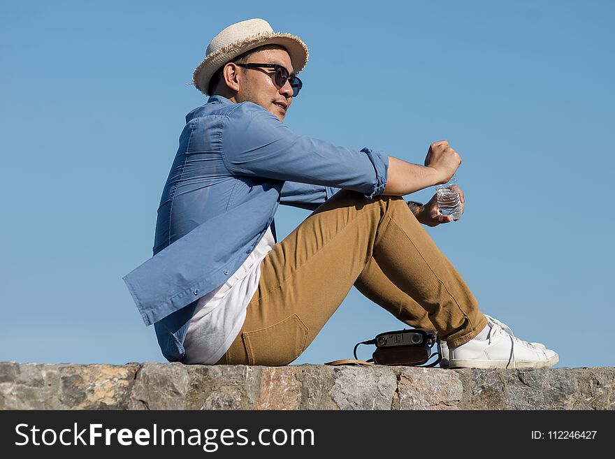 Asian Tourist Man Open A Bottle Of Water While Sitting Against