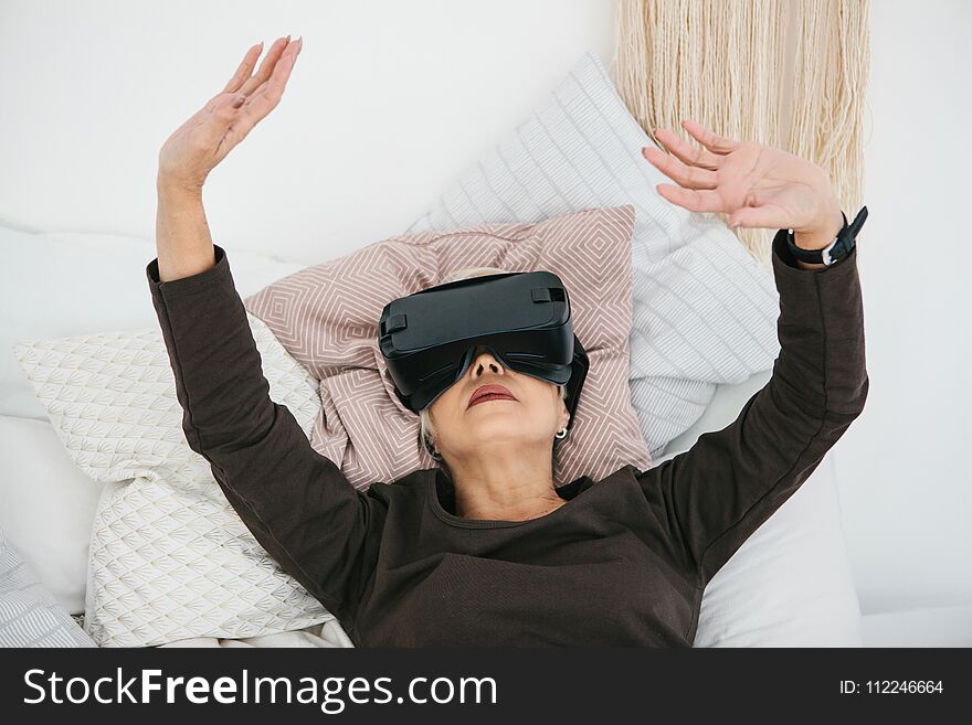 An elderly woman in virtual reality glasses. An elderly person using modern technology.