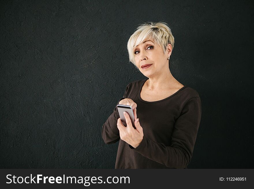 A Positive Modern Elderly Woman Is Holding A Cell Phone And Is Using It. The Older Generation And Modern Technology.