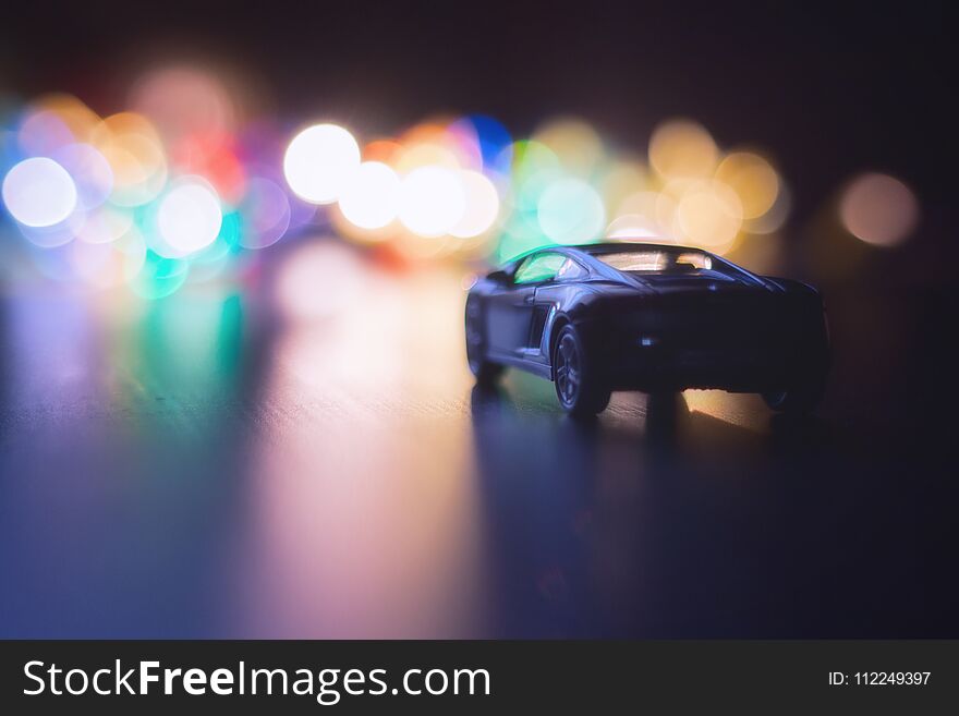 Small black car in dark night on the road and night multi-colored lights . the lights of the big city boheh , night traffic . car on night road. Small black car in dark night on the road and night multi-colored lights . the lights of the big city boheh , night traffic . car on night road