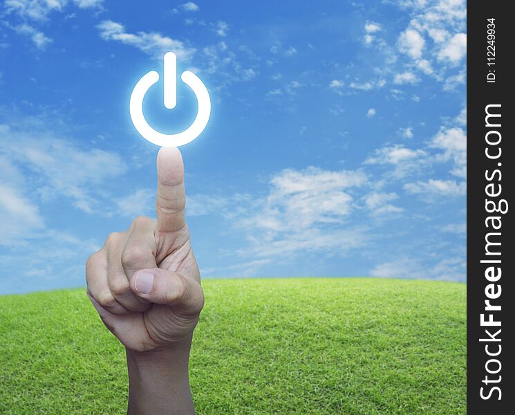 Hand pressing power button over green grass field with blue sky, Start up business concept