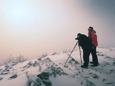 Hiker And Photo Enthusiast Stay On Snowy Peak At Tripod. Men On Cliff Speaking And Thinking. Stock Photography