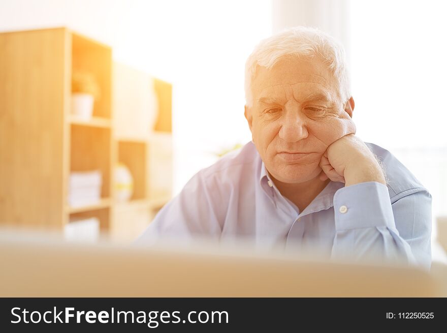 Aged pensive man working on computer in sunny room. Aged pensive man working on computer in sunny room