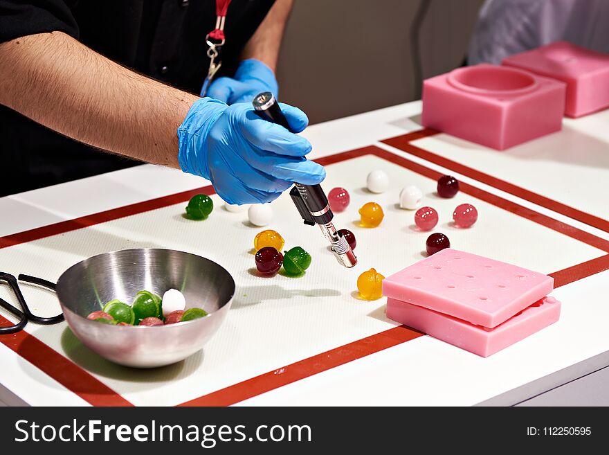 Confectioner with a burner prepares color sweet candy balls