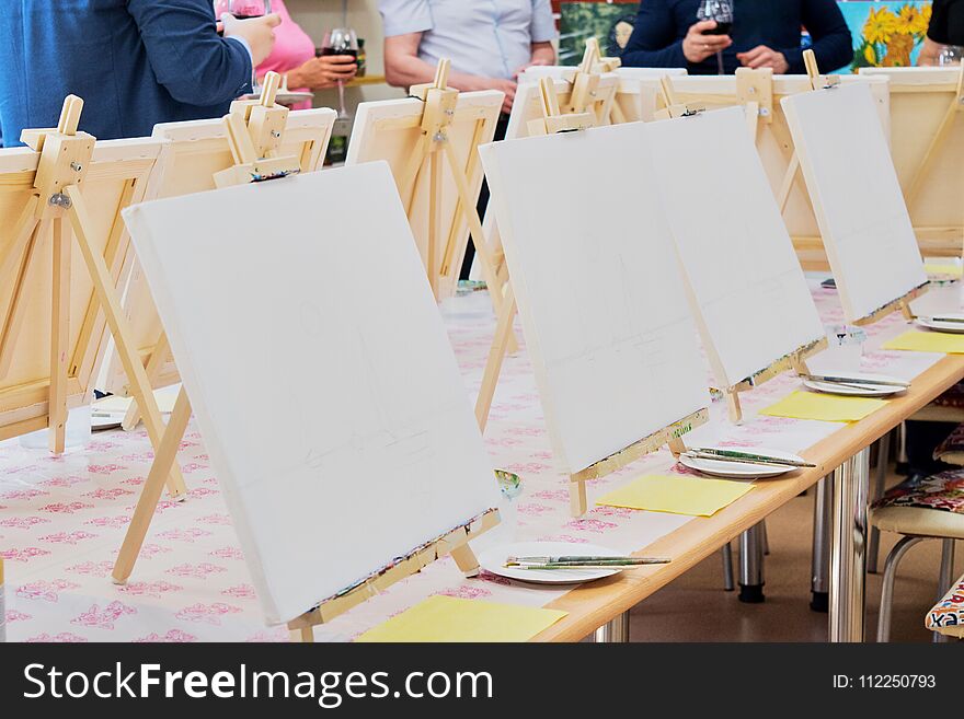 Canvases, brushes, palettes on the long wooden table ready for a masterclass in the art studio, people waiting to start drawing. Canvases, brushes, palettes on the long wooden table ready for a masterclass in the art studio, people waiting to start drawing