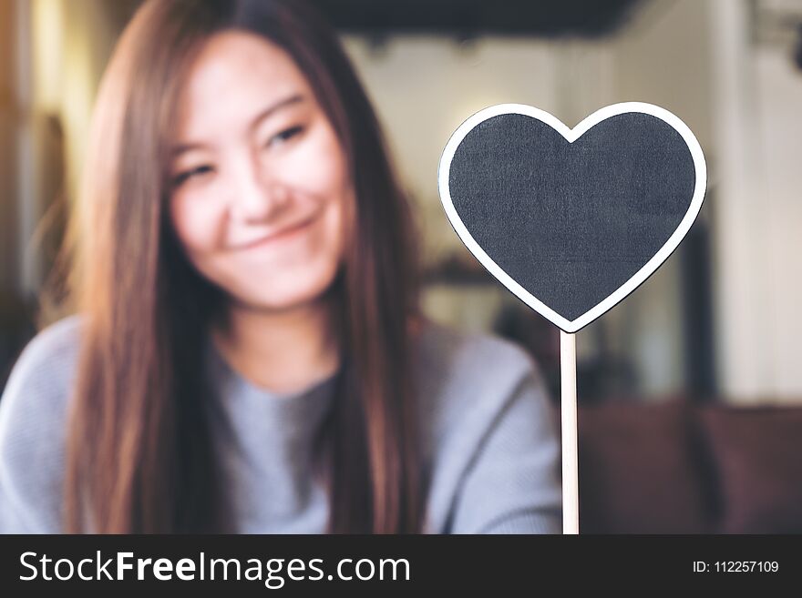 A beautiful asian woman holding a blank heart shape blackboard sign with feeling happy and in love