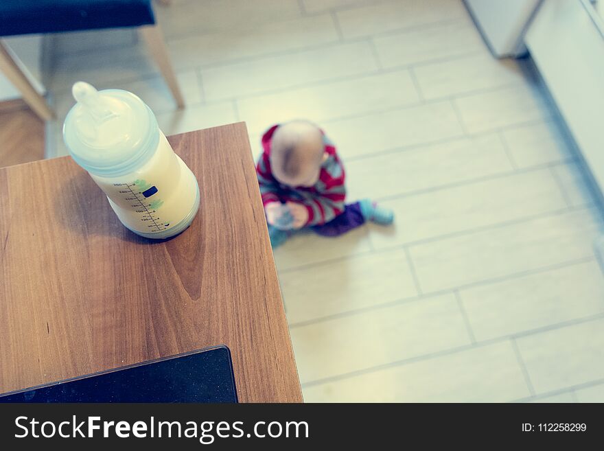 Baby playing in the kitchen. Warm milk ready to satisfy hunger.