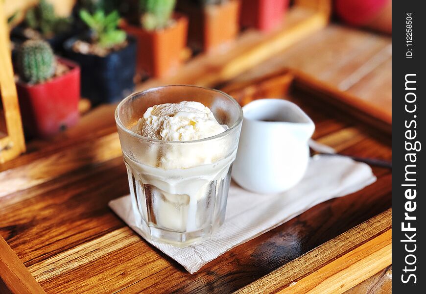 Espresso shot in white ceramic jar and Vanilla ice cream in glass on the wooden table with cactus background, Italian Iced Coffee Dessert name is `Affogato`.