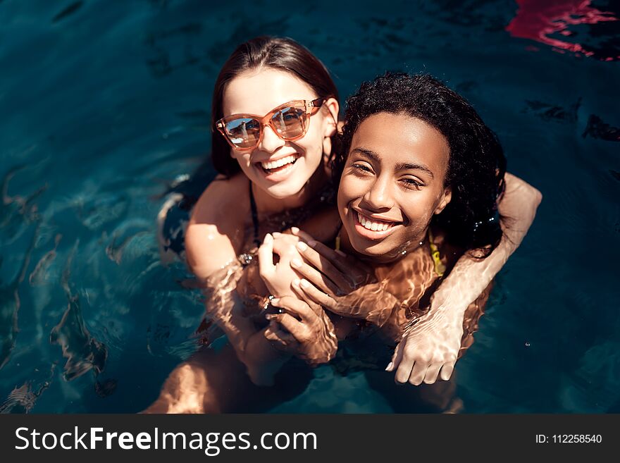 Two young girls in swimsuits have fun in swimming pool at summer time.