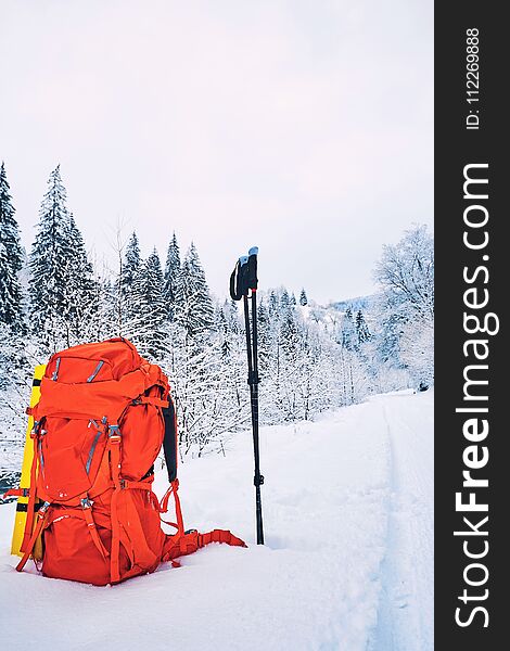 Red Backpack With Trekkingovymi Sticks On The Snow In The Background Of Mountains And Forests.