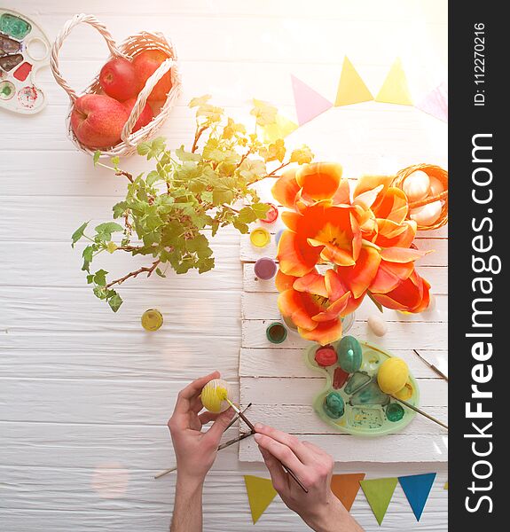 Man painting Easter eggs still life on a white wooden background.