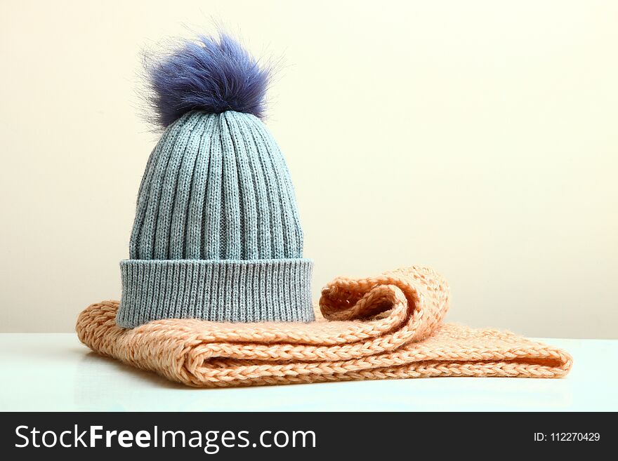 A beautiful gray hat with a pompon and a knitted scarf on a neutral background. A beautiful gray hat with a pompon and a knitted scarf on a neutral background.