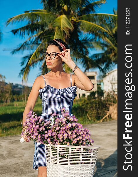 Pretty female in a blue dress riding a bicycle on palm background.