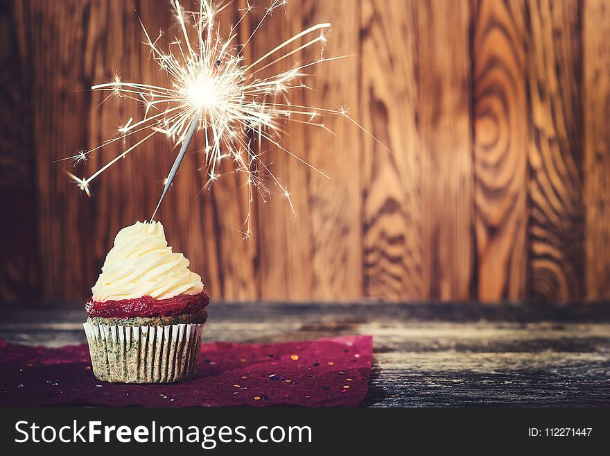 Cupcake with cream cheese, with sparkler on the dark wooden background.