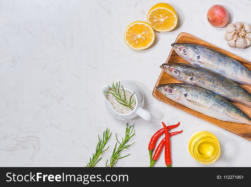 Fish dish cooking with various ingredients. Fresh raw fish decorated with lemon slices and herbs on wooden table.