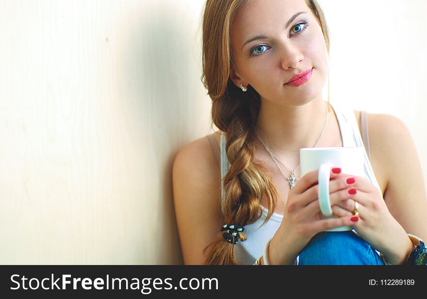 Beautiful woman sitting on the floor and holding a cup .