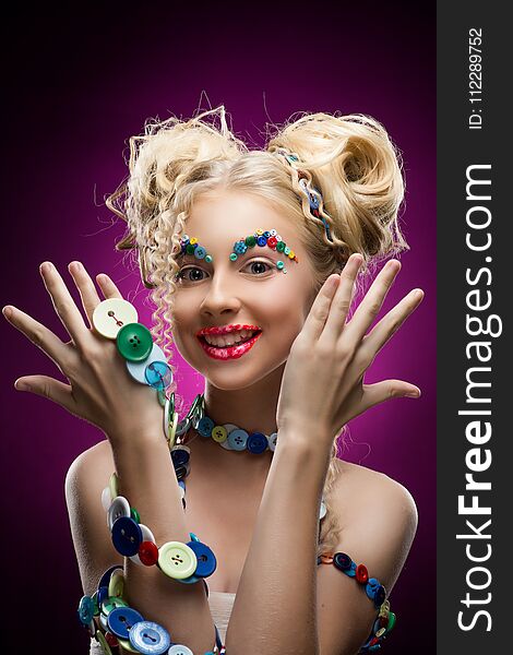 Smiling cute face nice blonde child girl wearing DIY bijou accessories made of multi-colored buttons shows her palms