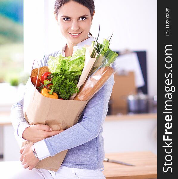 Young woman holding grocery shopping bag with vegetables . Standing in the kitchen.