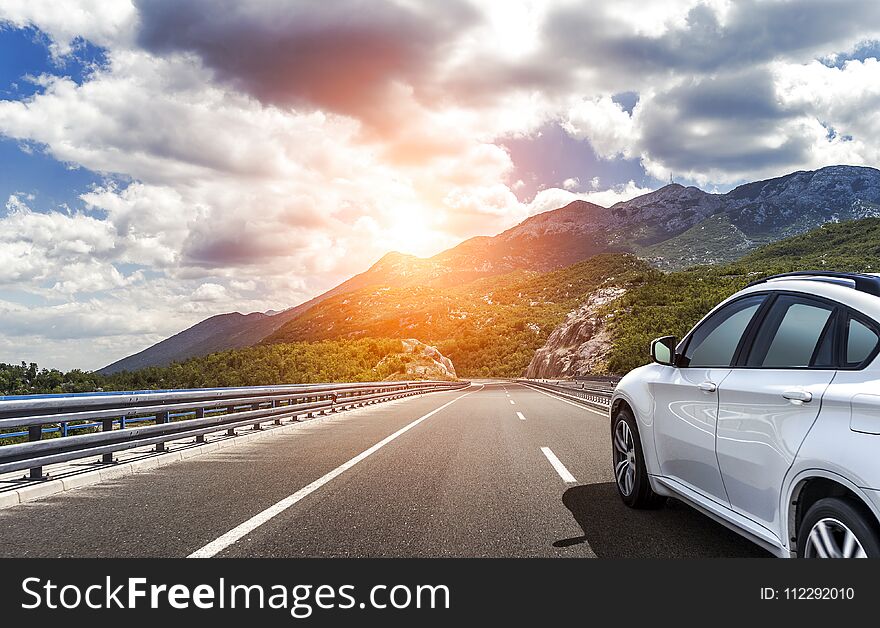 A white car rushing along a high-speed highway in the sun.