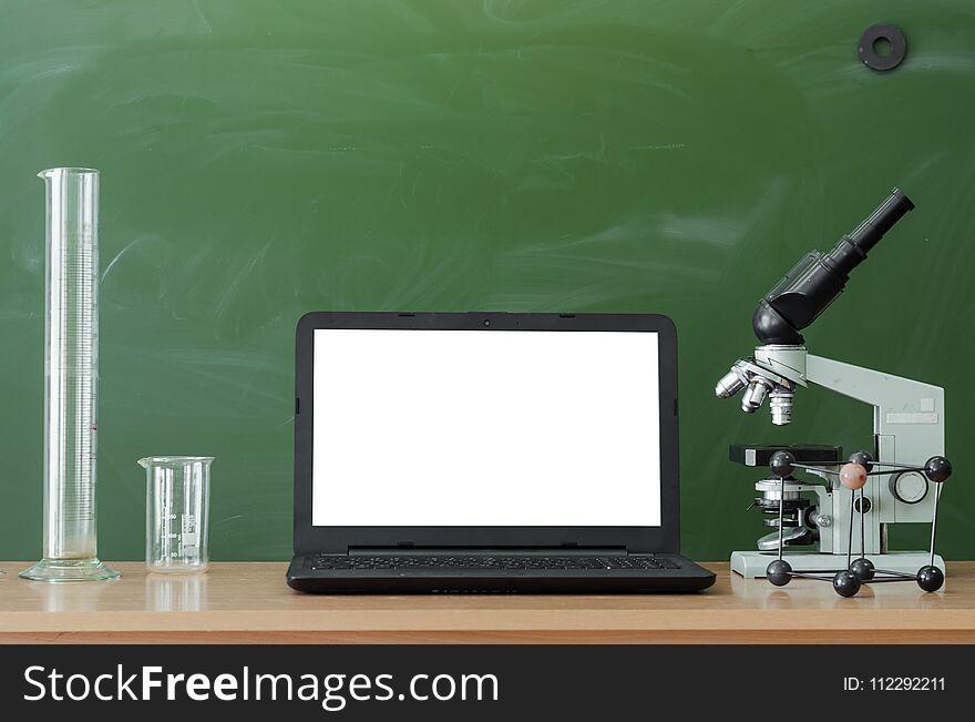 Teacher or student desk table. Education background. Education concept. Laptop with blank screen, microscope, flasks, beaker and molecule model on the table. Chemistry or biology lesson. Teacher or student desk table. Education background. Education concept. Laptop with blank screen, microscope, flasks, beaker and molecule model on the table. Chemistry or biology lesson.