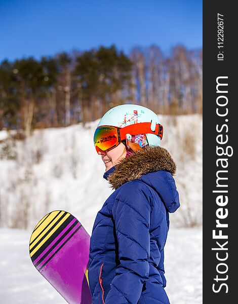 Side view of sporty woman wearing helmet with snowboard looking at camera