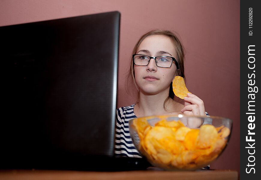 Young happy woman eating chips near a computer. Unhealthy concept.
