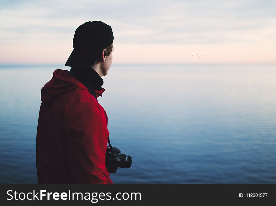 Man In Red Jacket Standing Near Body Of Water