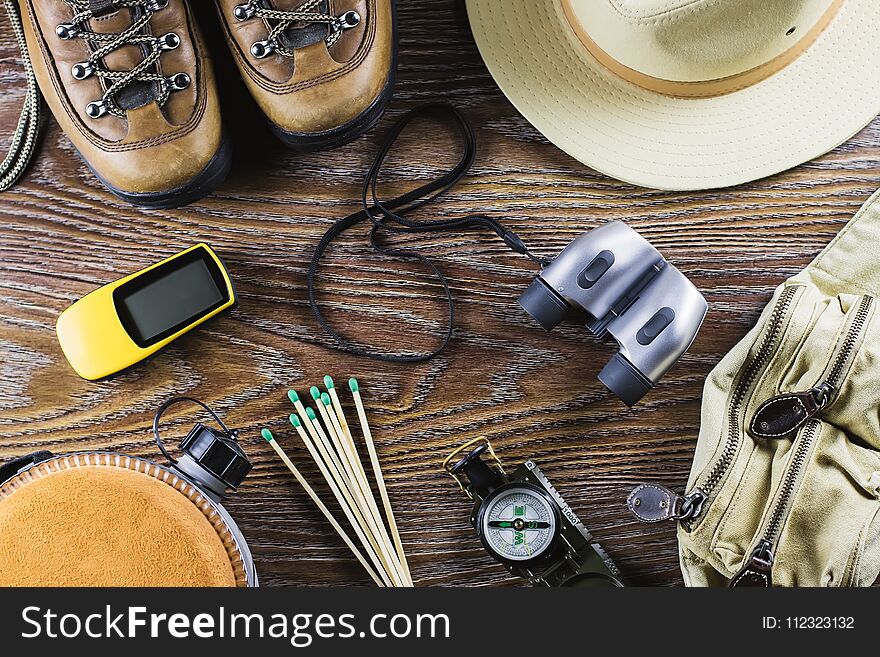 Hiking or travel equipment with boots, compass, binoculars, matches on wooden background. Active lifestyle concept. Top view