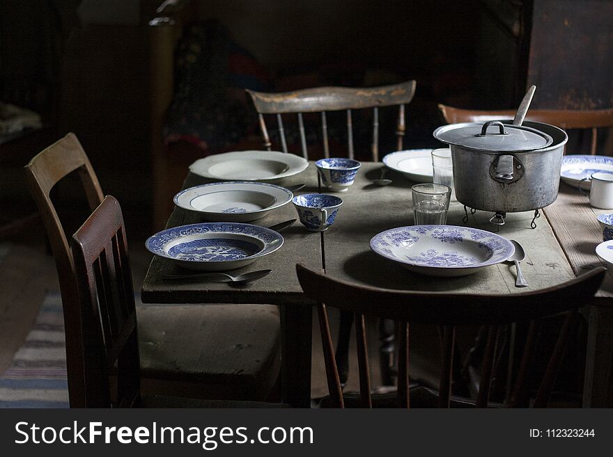 Vintage Set Table With Old Plates And Wooden Chairs In A Poor Interior
