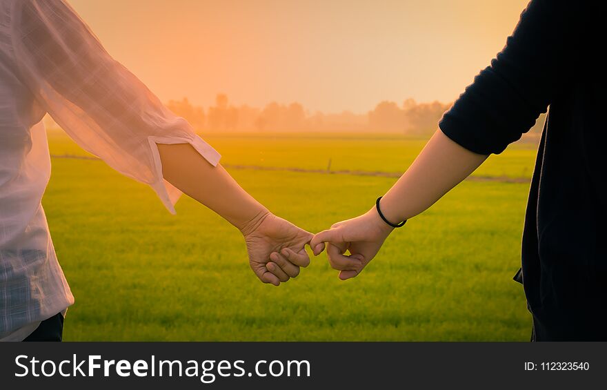 Close up Two Asian women wearing white and black shirts stand be hand in hand and look at the green Field morning light.