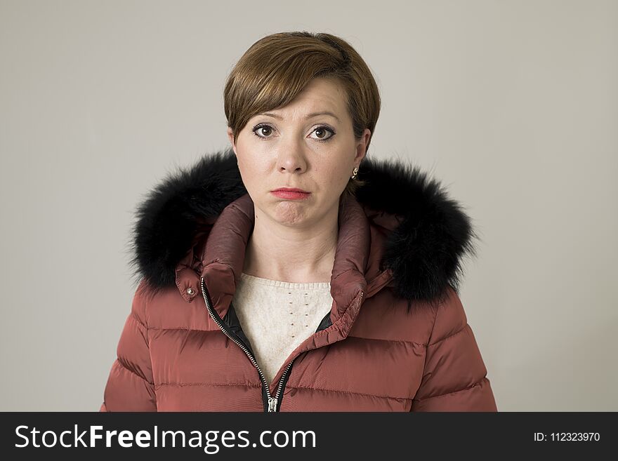 Young sweet and sad red hair woman posing moody and depressed looking to camera wearing warm winter coat jacket with hood isolated on gray background
