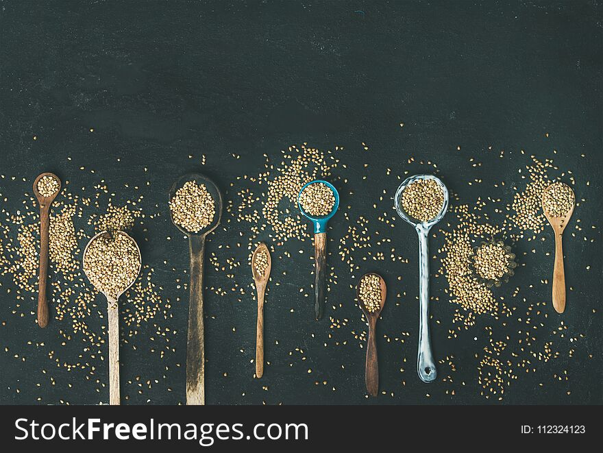 Flat-lay of various old vintage kitchen spoons full of green uncooked buckwheat grains over black stone background, top view, copy space, horizontal composition. Rustic cooking concept. Flat-lay of various old vintage kitchen spoons full of green uncooked buckwheat grains over black stone background, top view, copy space, horizontal composition. Rustic cooking concept