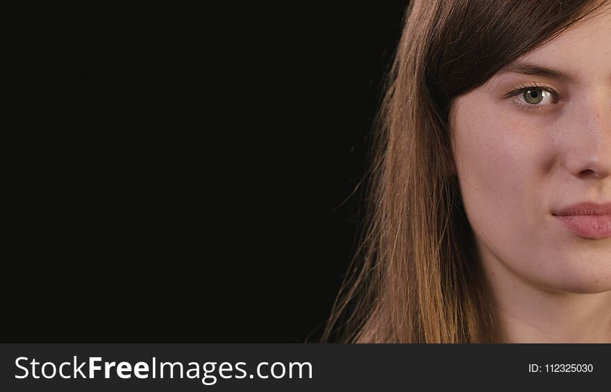A beautiful young lady`s half face smiling against a black background. Close-up shot. A beautiful young lady`s half face smiling against a black background. Close-up shot