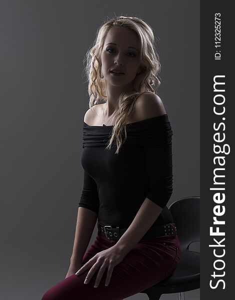 Beautiful blond woman in curly hair and black top and red pants on a grey background