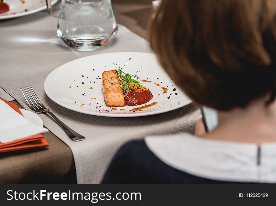 Woman eats delicious salmon in a restaurant. small portion on a white plate. Food and wine tasting