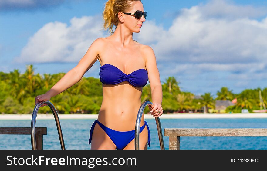 Woman In Blue Bikini Wearing Sunglasses On A Tropical Beach Background